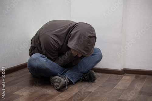 desperate young drug addict wearing hood and sitting alone in corner © dashtik
