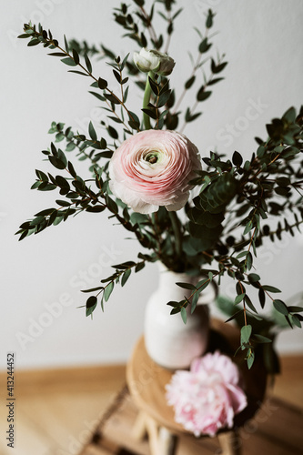 lockerer moderner Blumenstrauß mit rosa Ranunkel und Eukalyptuszweigen in einer Keramikvase auf einem Holzhocker von oben