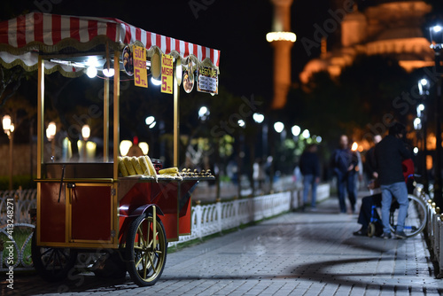 Traditional cart of Turkish street food in night near with Blue Mosque. Text on signboards in translation from Turkish language on English - Corn in the embers and milk corn. photo