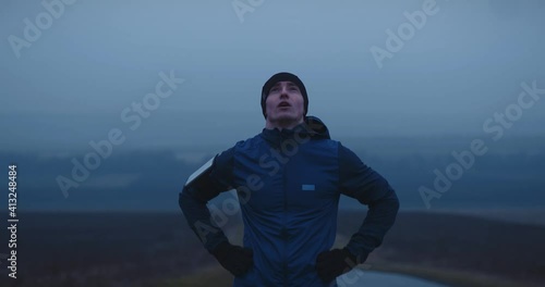 Young male athlete stopped to rest and catch breath after running long distance. Exhausted spotsman amateur standing outdoors, breathing hard. photo