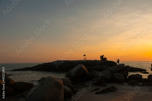 The stones on beach in evening have the background of the sea and the evening sun. There are people standing on rocks and flags © WP_7824