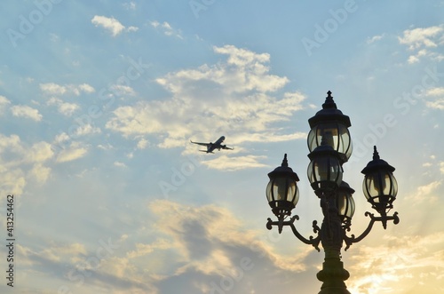 Lanterns against a blue sky with a flying plane. © Tetiana
