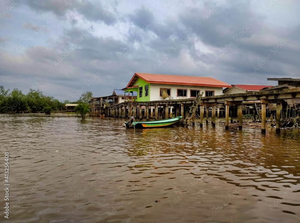Fototapeta premium Houses on wooden piles. Boat pier. Brown water. Binsuluk Forest Reserve. State of Sabah on the island of Borneo. Malaysia. South-East Asia