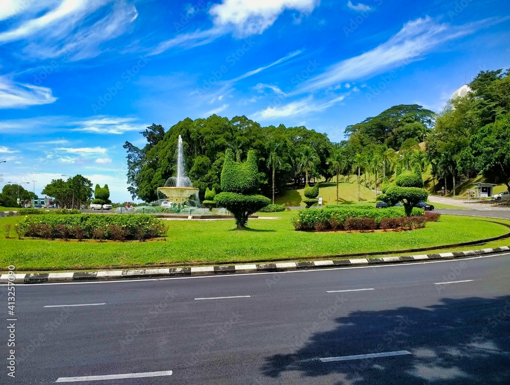 Road view in Kuching city. Flowerbeds with tropical vegetation and a fountain. Borneo Island. Sarawak. Malaysia. South-East Asia