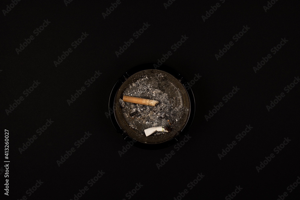 Dirty ashtray full of cigarette with smoke Isolated on a black background, view from above. Dirty ashtray full of cigarette with smoke Isolated on a black background, view from above.