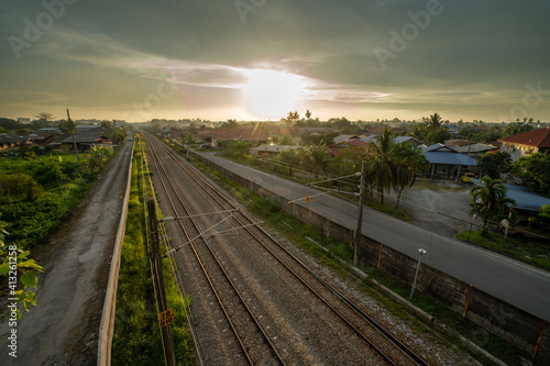 Train railway road in the middle of village with bright sun and cloudy day © Sufian