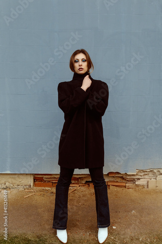 Caucasian woman, model, posing and looking at the camera, with an street underground wall in the background. Fashion, editorial and model concept.