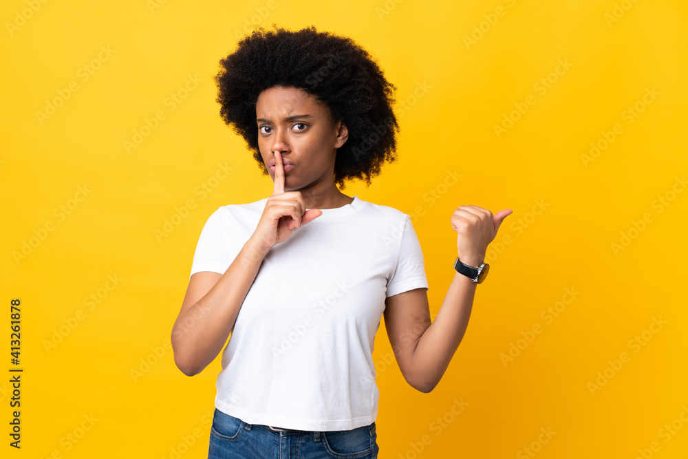 Young African American woman isolated on yellow background pointing to the side and doing silence gesture