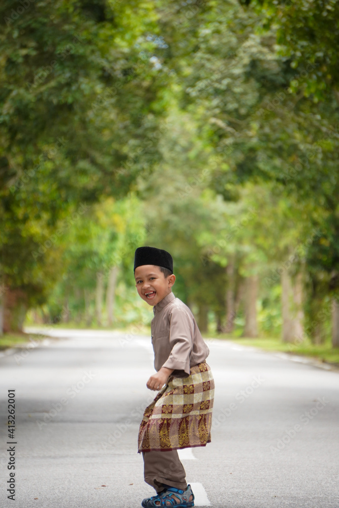 A Malay boy in Malay traditional cloth showing his happy reaction during Eid Fitri or Hari Raya celebration. A Malay boy in Malay traditional cloth showing his happy reaction during Eid Fitri or Hari Raya celebration.