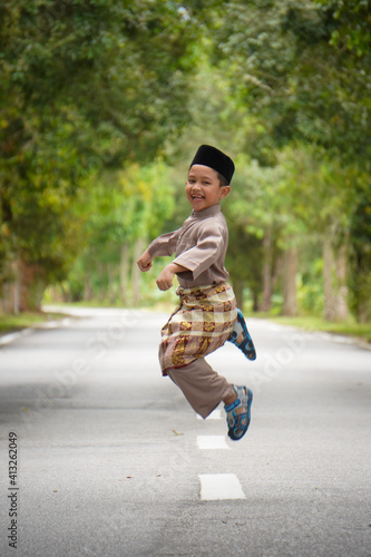 A Malay boy in Malay traditional cloth showing his happy reaction during Eid Fitri or Hari Raya celebration.