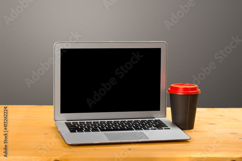 mocap Laptop with blank screen for product display and coffee on a wooden table.