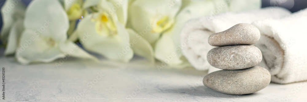 Fototapeta premium Banner of spa resort therapy composition with massage stones, rolled towels, and orchid flowers, abstract lights. Concept of spa, relax or resort.