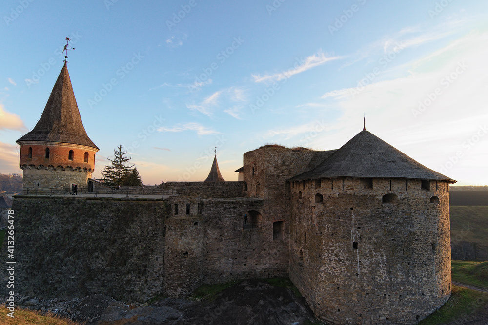 Close up view of medieval Kamianets-Podilskyi Castle. Thick stone walls and tall towers. Colorful vibrant sky during sunset. Famous touristic place and romantic travel destination. Ukraine