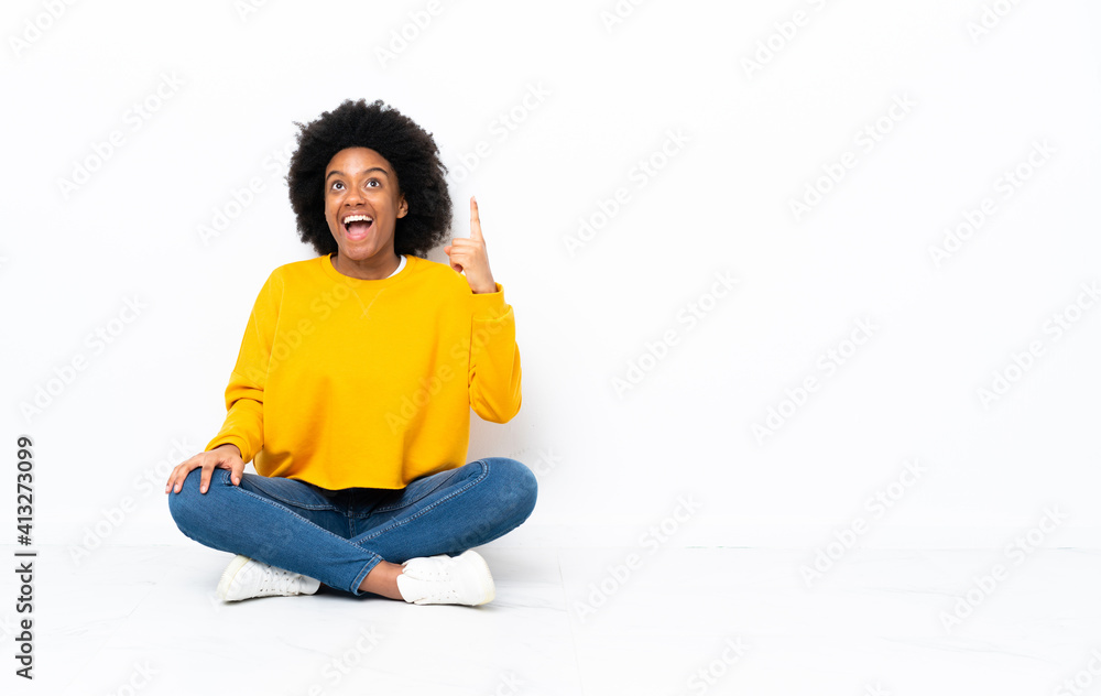 Young African American woman sitting on the floor pointing up and surprised Young African American woman sitting on the floor pointing up and surprised