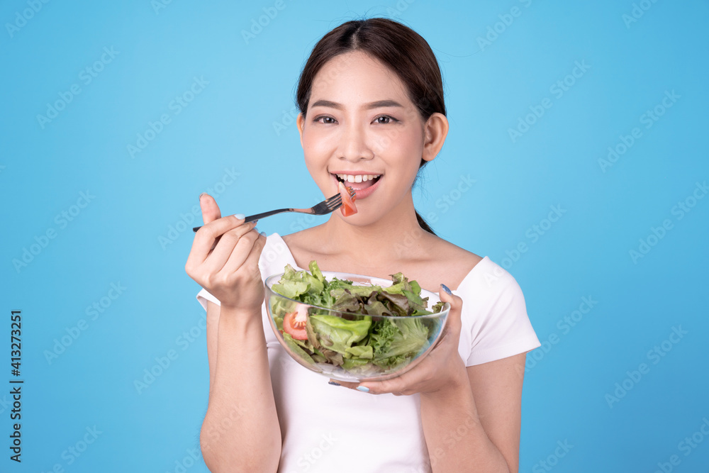 Young beautiful Asian woman eating a salad, Isolated on blue background. Young beautiful Asian woman eating a salad, Isolated on blue background.