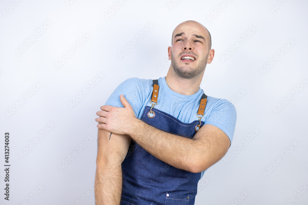 Young bald man wearing apron uniform over isolated white background with pain on his shoulder and a painful expression Young bald man wearing apron uniform over isolated white background with pain on his shoulder and a painful expression