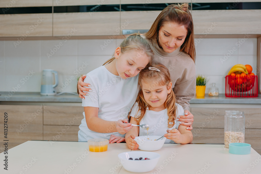 A mom and her two daughters add honey to oatmeal in the kitchen.