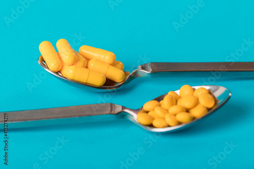 Table spoons filled with assortment of yellow pills isolated on blue  coloured background. Medication and prescription pills flat lay background. Antiobesity medication and dieting. photo