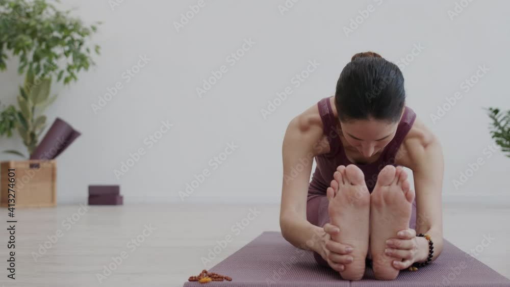 Lockdown of beautiful Caucasian woman wearing sportswear sitting on rubber mat in stretching studio and stretching her legs muscles Lockdown of beautiful Caucasian woman wearing sportswear sitting on rubber mat in stretching studio and stretching her legs muscles