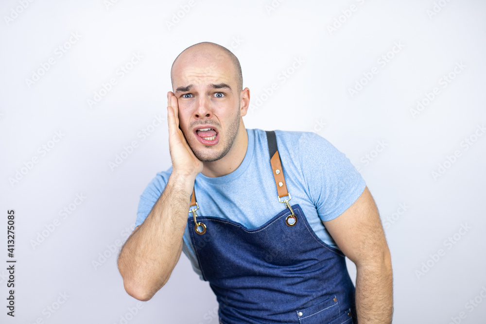 Young bald man wearing apron uniform over isolated white background touching mouth with hand with painful expression because of toothache or dental illness on teeth Young bald man wearing apron uniform over isolated white background touching mouth with hand with painful expression because of toothache or dental illness on teeth