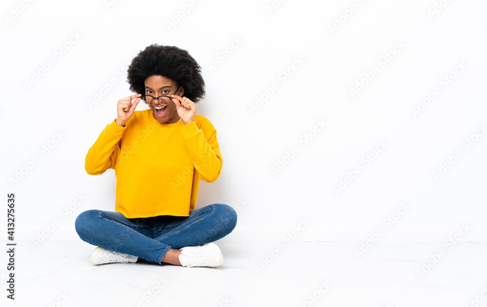 Young African American woman sitting on the floor with glasses and surprised Young African American woman sitting on the floor with glasses and surprised