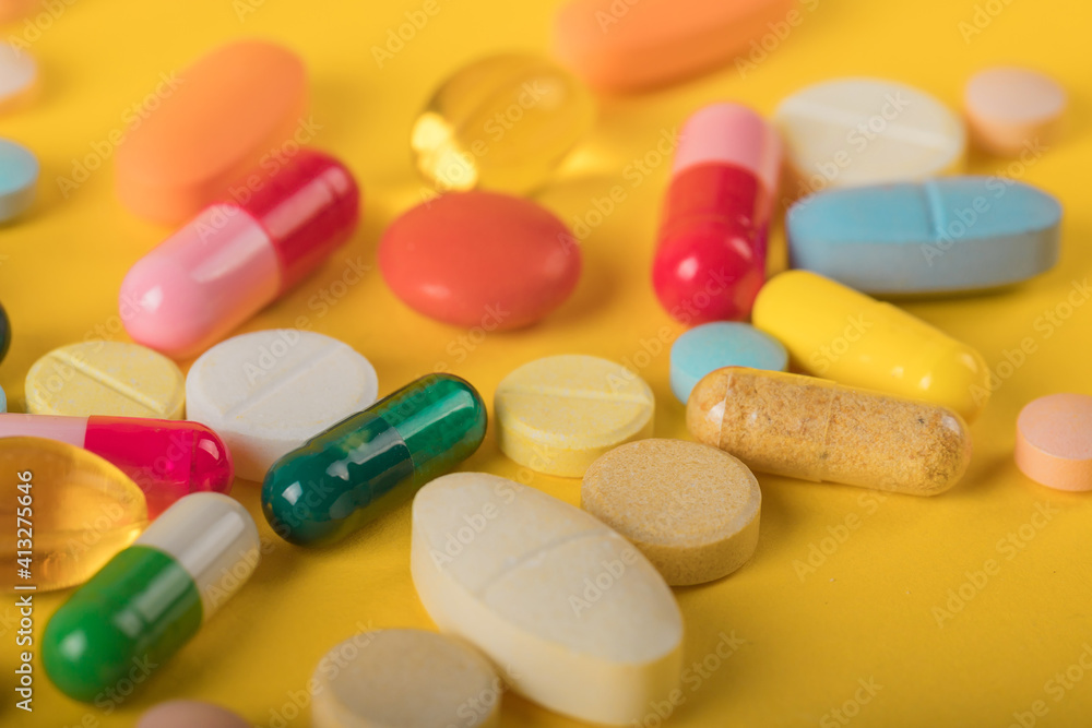Assorted pharmaceutical medicine pills, tablets and capsules over yellow background. High number of pills on surface. High resolution image for pharmaceutical industry. Assorted pharmaceutical medicine pills, tablets and capsules over yellow background. High number of pills on surface. High resolution image for pharmaceutical industry.