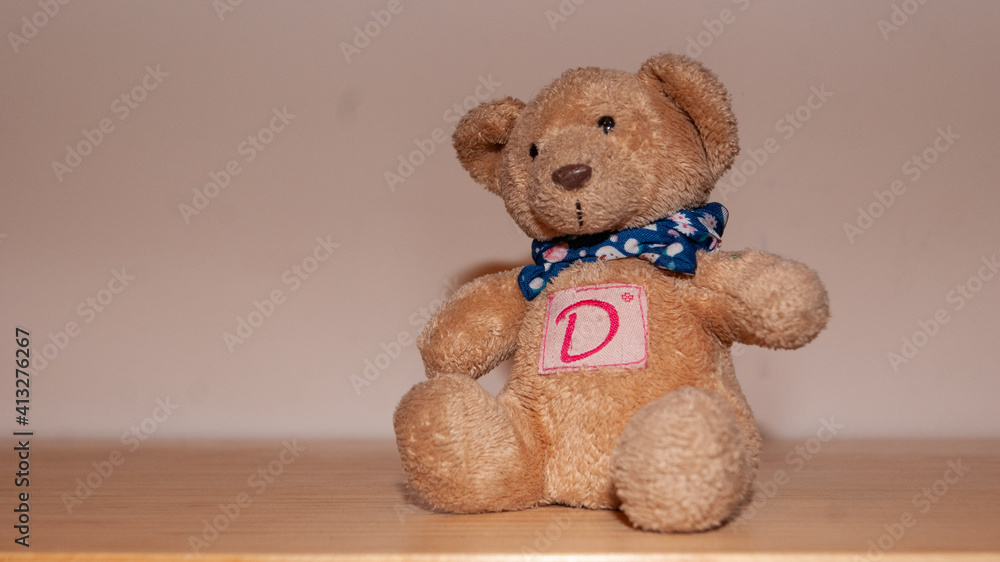 Osito de peluche con una letra "D" en el pecho sentado sobre mesa de madera  foto de Stock | Adobe Stock