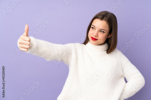 Teenager girl isolated on purple background giving a thumbs up gesture