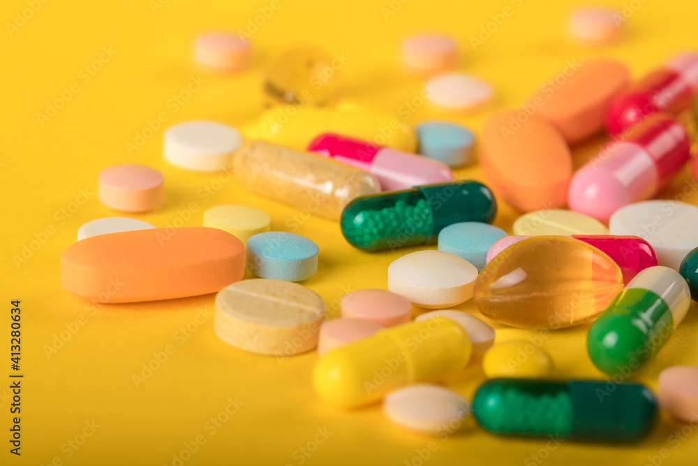 Assorted pharmaceutical medicine pills, tablets and capsules over yellow background. High number of pills on  surface. High resolution image for pharmaceutical industry.