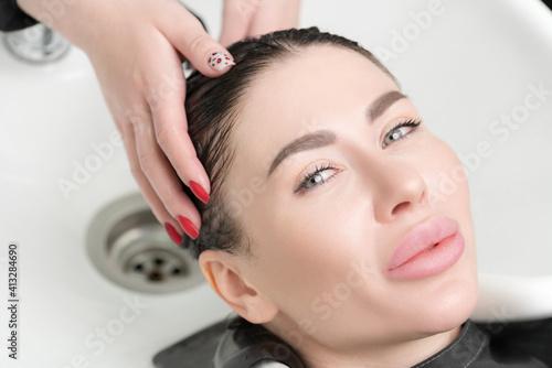 Hairdresser's hands wash long hair of beautiful brunette woman with shampoo in special sink for shampooing in hair and beauty salon.