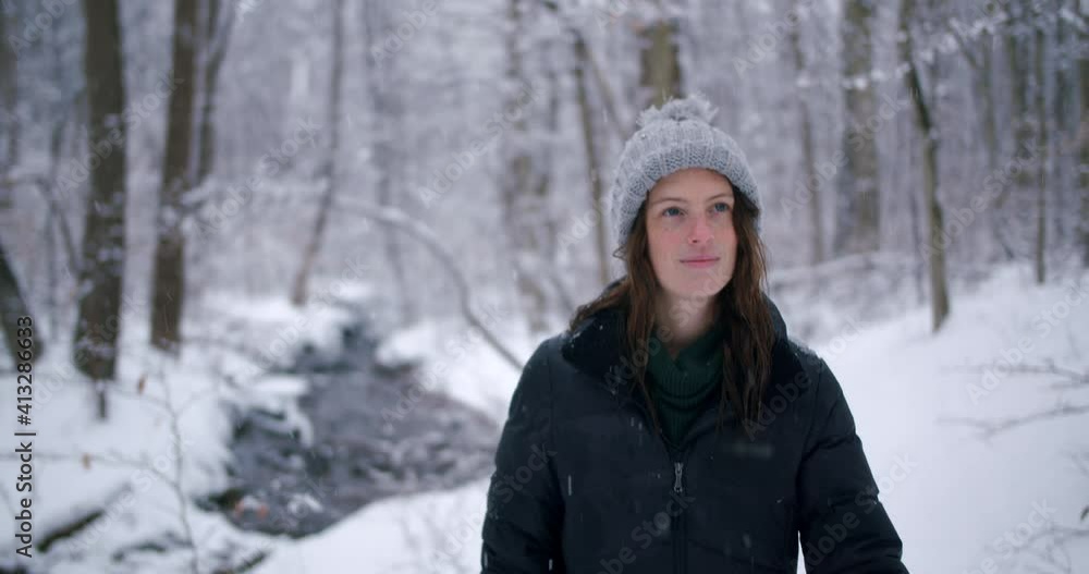 Young woman hiking through snowy forest with stream in the background, happy and reflective Young woman hiking through snowy forest with stream in the background, happy and reflective