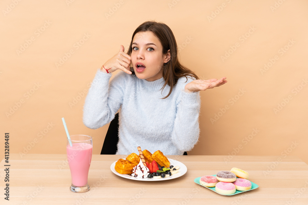 Teenager girl eating waffles isolated on beige background making phone gesture and doubting
