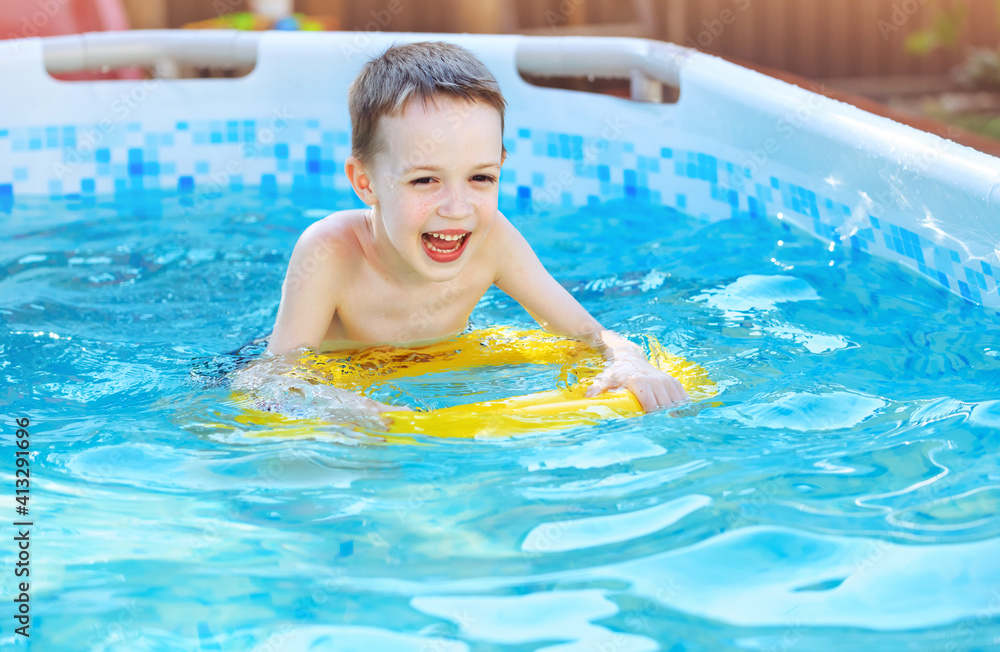 Little boy is splashing with inflatable toy in swimming pool outdoor, having fun. Kids learn to swim
