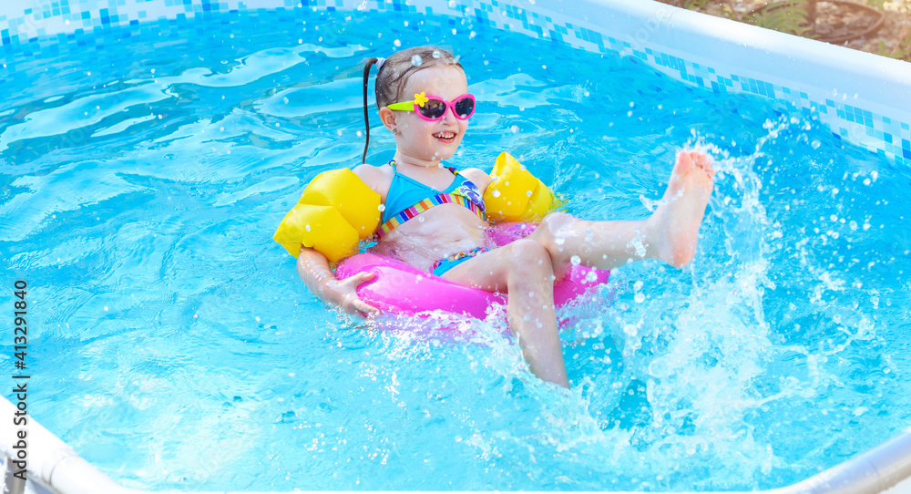 Little girl is splashing in frame swimming pool outdoor at home garden