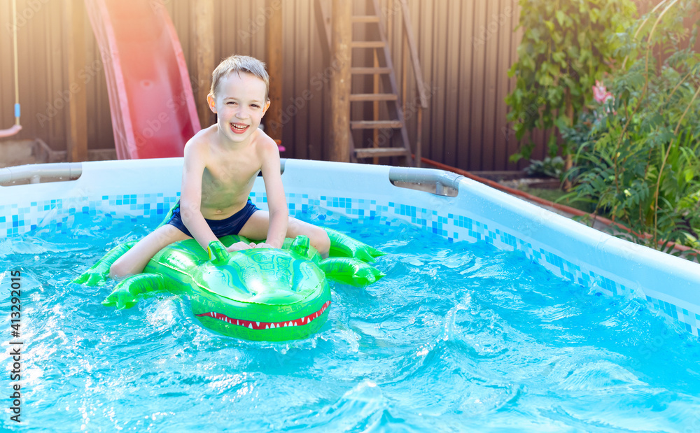 Boy on inflatable crocodile float in outdoor swimming pool at home
