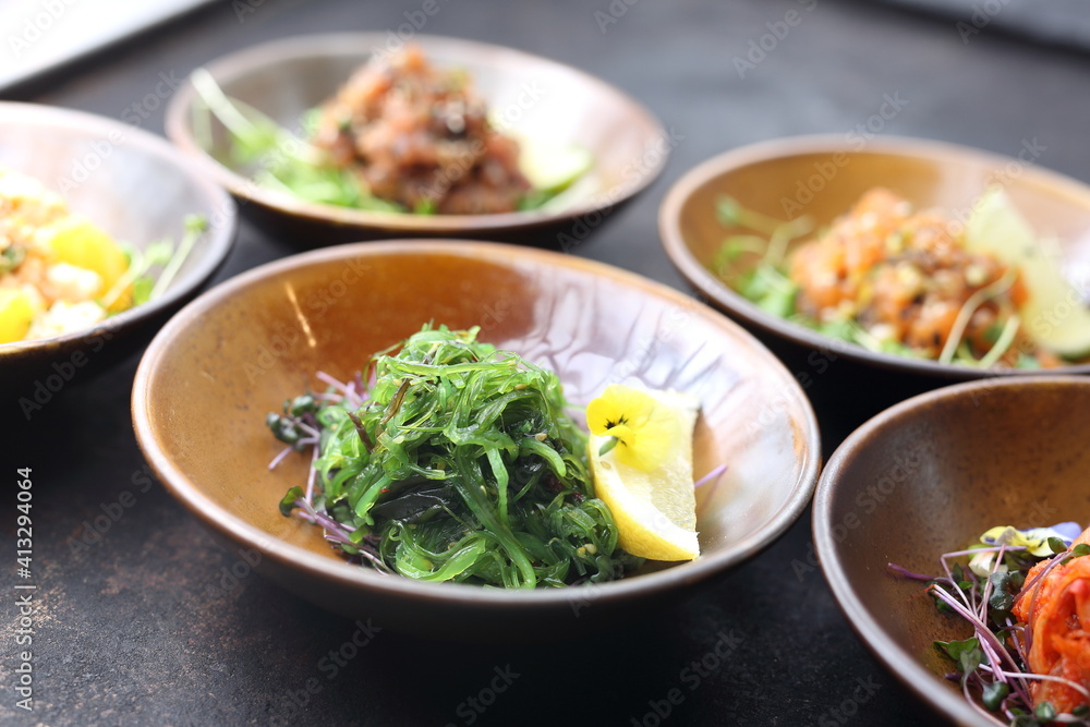 Japanese seaweed salad on a black stony background, a composition of appetizers in a background. Japanese seaweed salad on a black stony background, a composition of appetizers in a background.