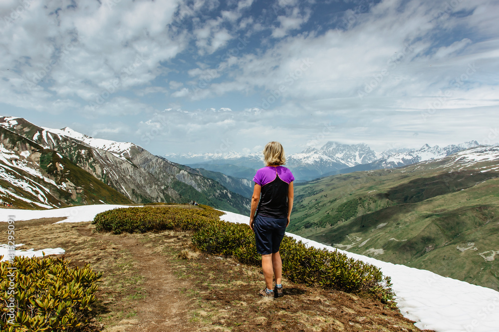 Girl standin on the top of a mountain,Georgia, snowy peaks in background.Backpacker enjoying view of mountain panorama.Wanderlust travel scene.Sporty woman on the summit.Adventure freedom concept