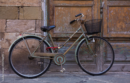 An classic, old, vintage bicycle with wicker basket rests against a weathered wall and door in Lucca, Italy 