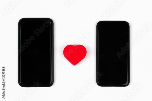 Red heart between two mobile phones on white background. Internet dating, copy space, Valentines day concept.