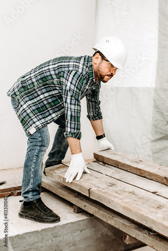 Man builder rearranges wooden beams at construction site