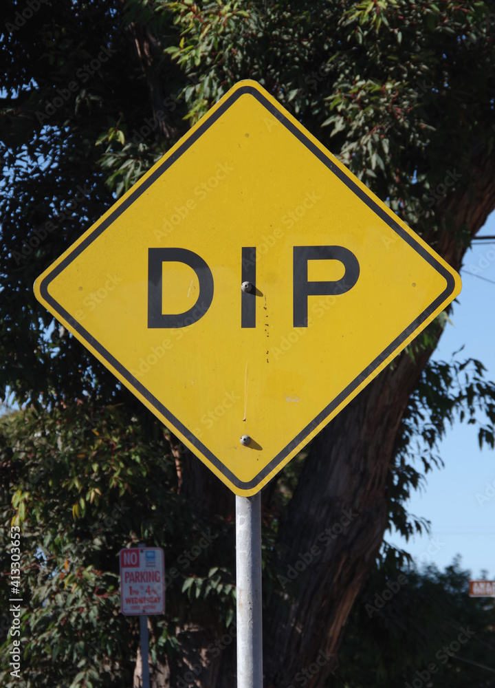 Close-up view of a yellow and black traffic sign warning of a  DIP in the road
