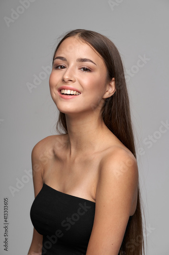 Young beautiful female model close-up studio beauty portrait. Girl with natural make-up and long brunette straight hair. Happy smiling woman looking at you