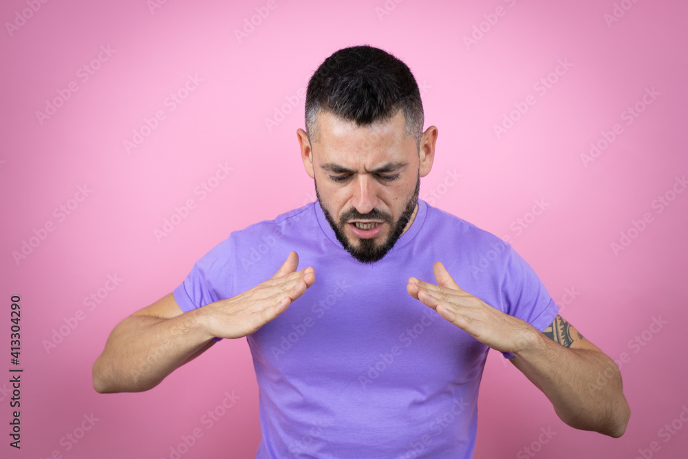 Young handsome man wearing casual t-shirt over pink background shouting and screaming loud down with hands on mouth Young handsome man wearing casual t-shirt over pink background shouting and screaming loud down with hands on mouth