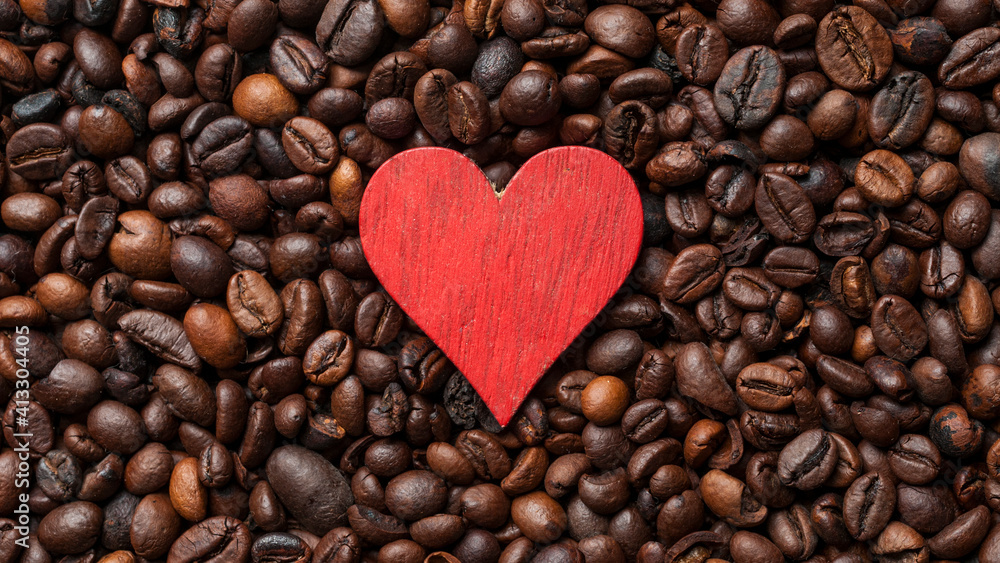 Red wooden heart resting on a bed of fresh roasted coffee beans Red wooden heart resting on a bed of fresh roasted coffee beans