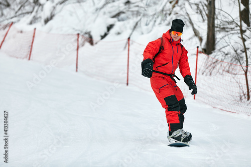 Male snowboarder in a red suit rides on the snowy hill with snowboard, Skiing and snowboarding concept