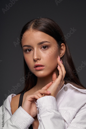 Close-up breast-up portrait of young beautiful brunette teenager girl with long straight hair and perfect natural make-up posing against grey background photo