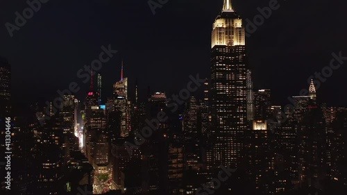 AERIAL: Breathtaking wide view the iconic Empire State Building disappearing behind residential condominiums and office buildings in Midtown Manhattan, New York City at night Circa September 2019