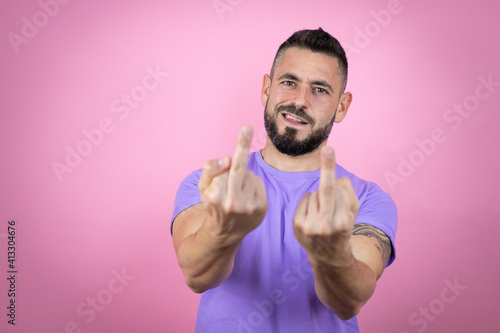 Young handsome man wearing casual t-shirt over pink background showing middle finger doing fuck you bad expression, provocation and rude attitude. screaming excited © Irene