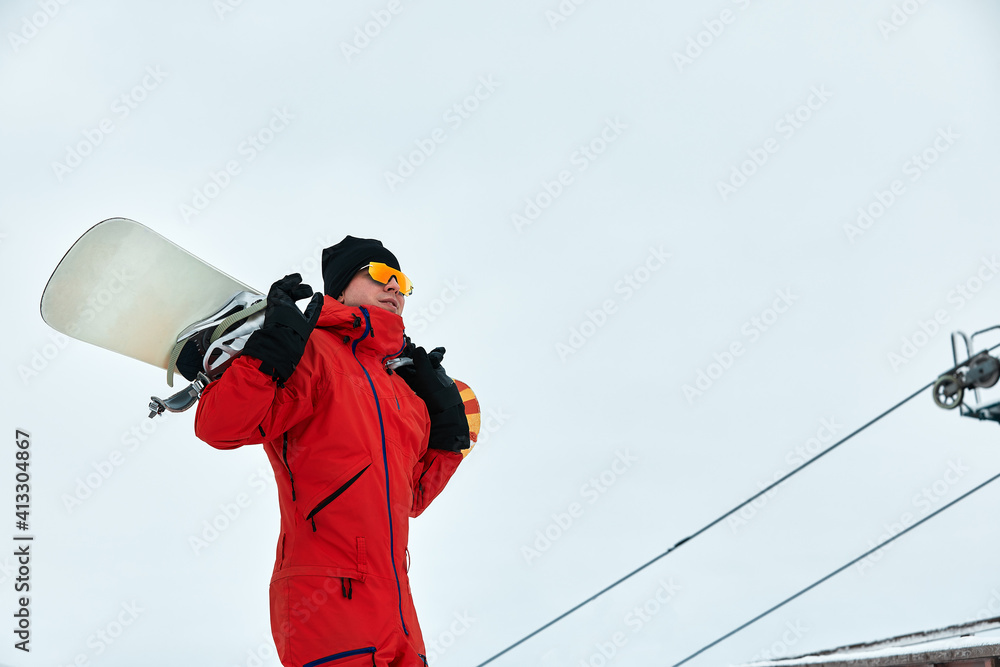 Male snowboarder in a red suit walking on the snowy hill with snowboard, Skiing and snowboarding concept