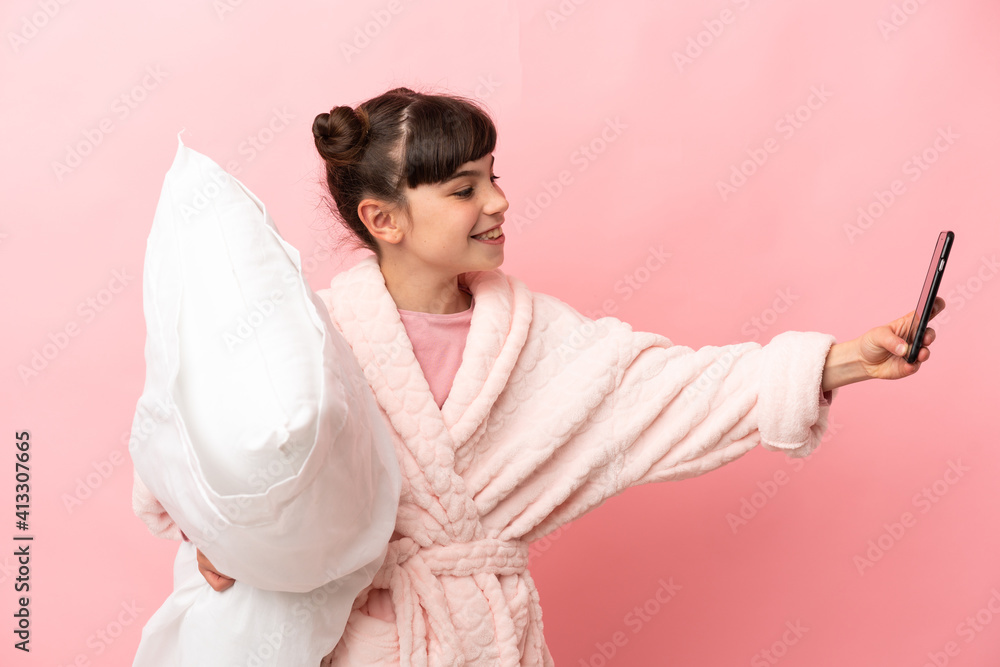 Little caucasian girl isolated on pink background in pajamas and holding a pillow while making a selfie Little caucasian girl isolated on pink background in pajamas and holding a pillow while making a selfie